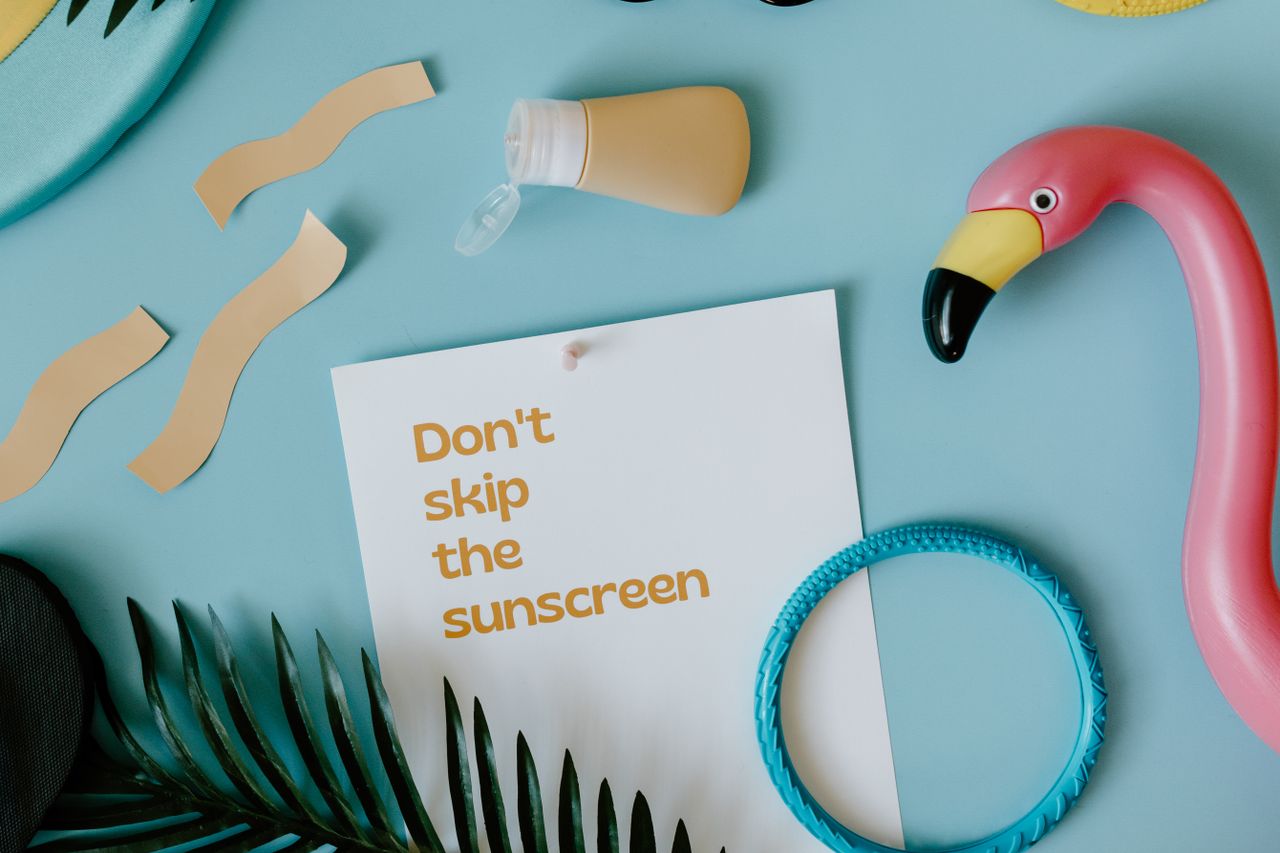 Flat lay of beach essentials with a whimsical note reminding about sunscreen application.