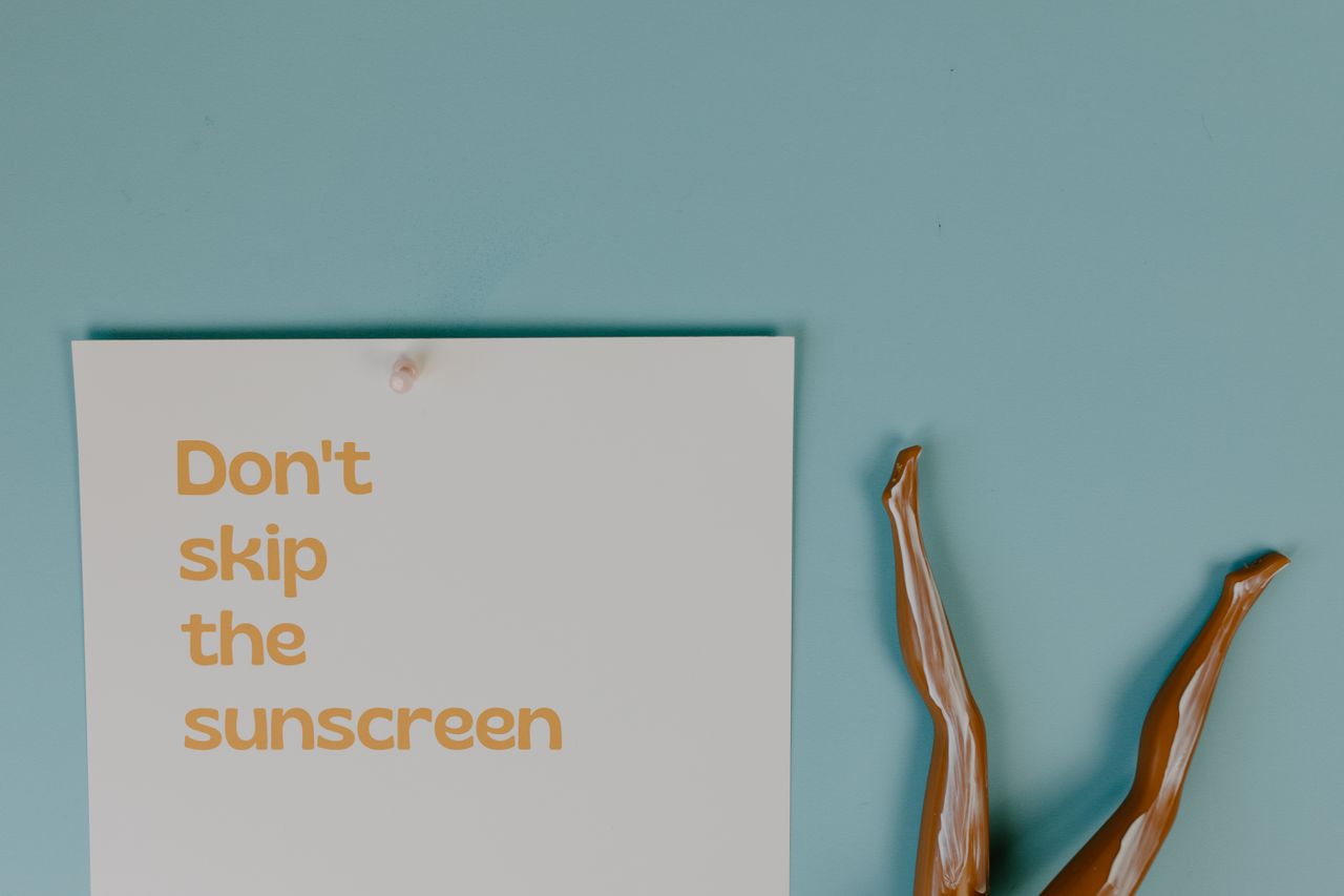 Creative flat lay with a sunscreen reminder and mannequin legs on a blue background.